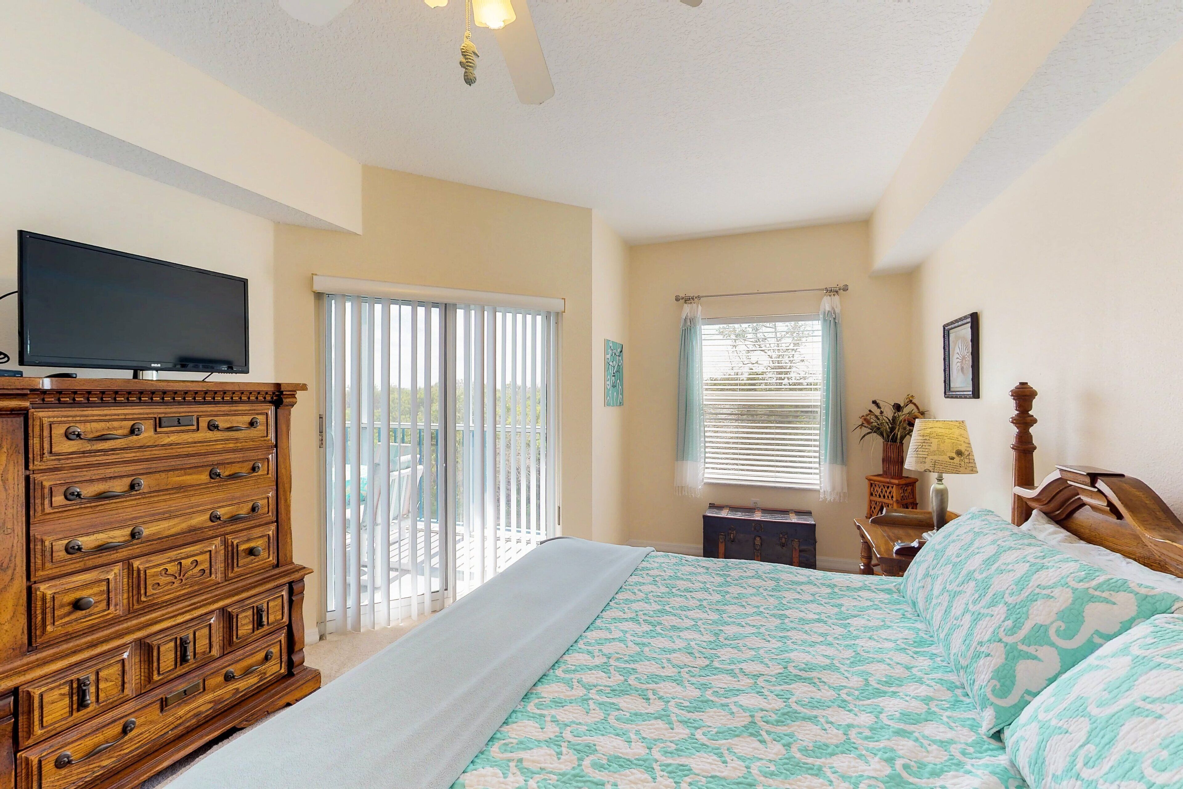 A bedroom with a large bed, a wooden dresser, a television, and a window with blinds.