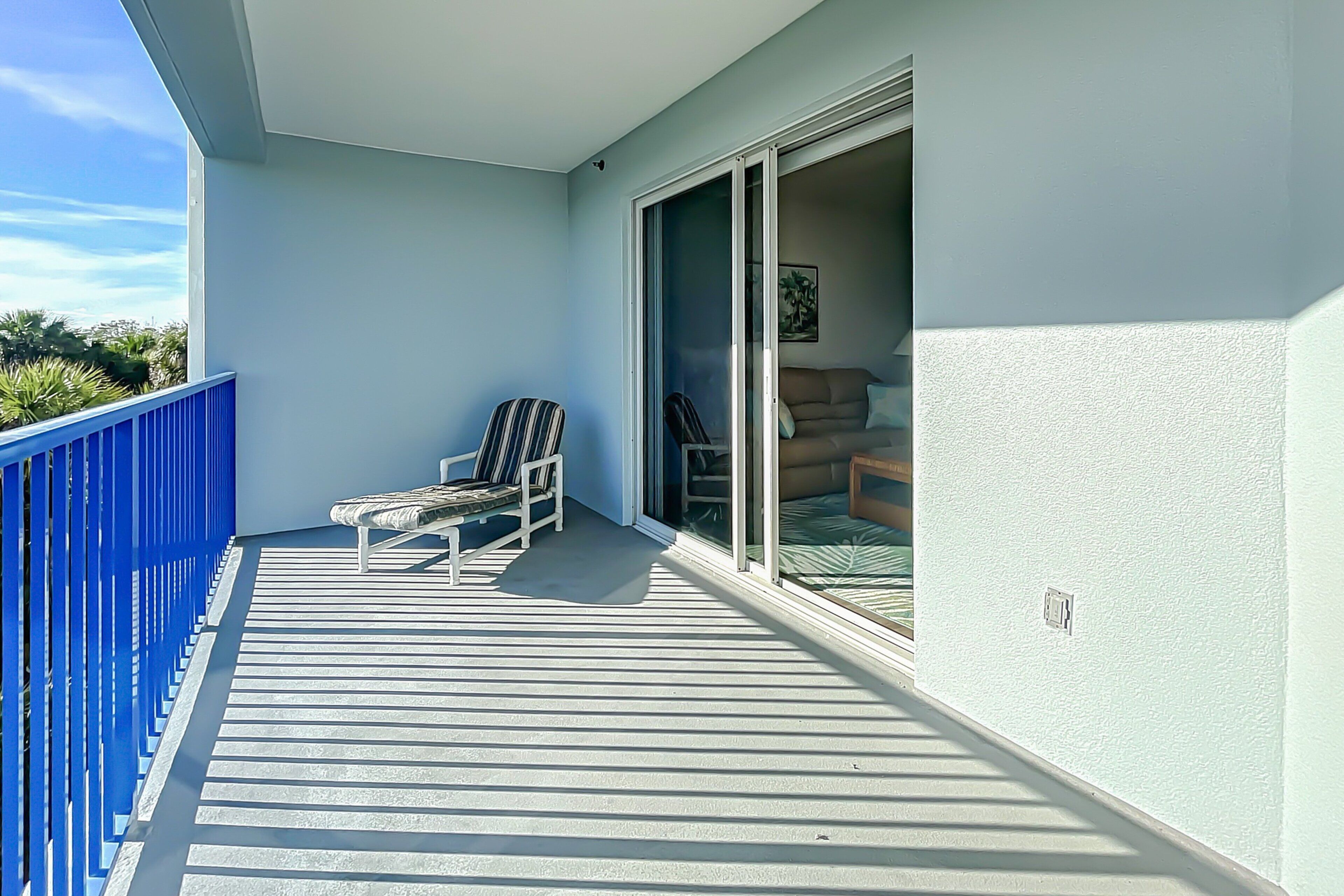 A balcony with a blue railing, a striped chair, and a sofa with a green cushion.