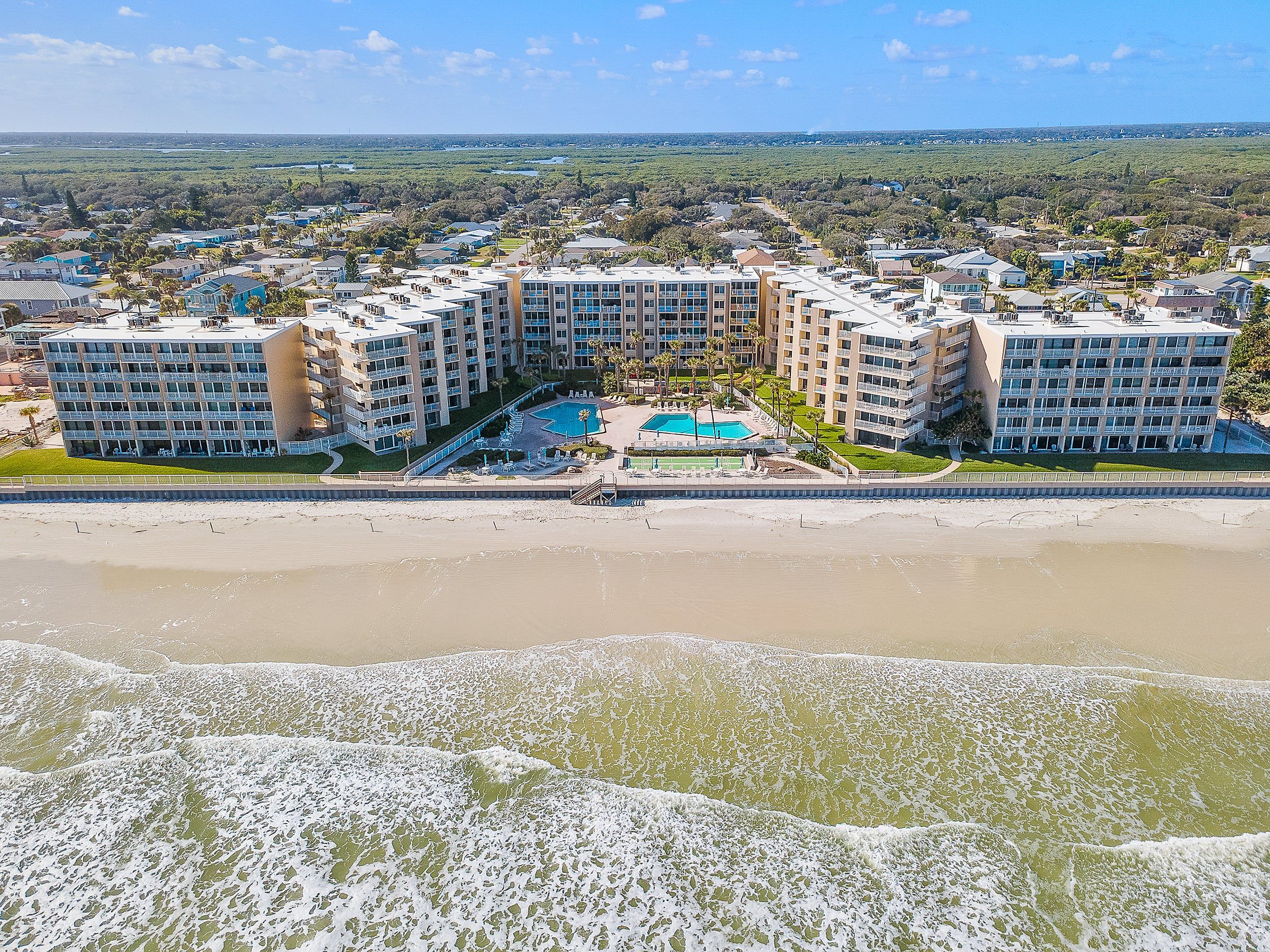 A beachfront hotel with multiple buildings, a swimming pool, and a beach in the foreground.