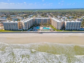 A beachfront hotel with multiple buildings, a swimming pool, and a beach in the foreground. - Pelican (New Smyrna Beach)