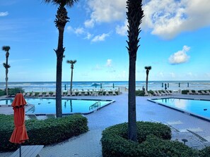 Ett poolområde med två pooler, solstolar, palmer och utsikt över havet.