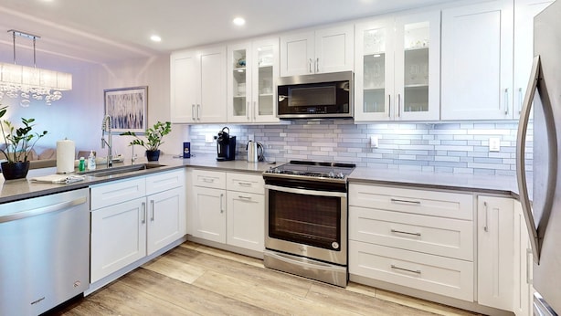 Una cocina moderna con armarios blancos, una estufa de acero inoxidable y un microondas.