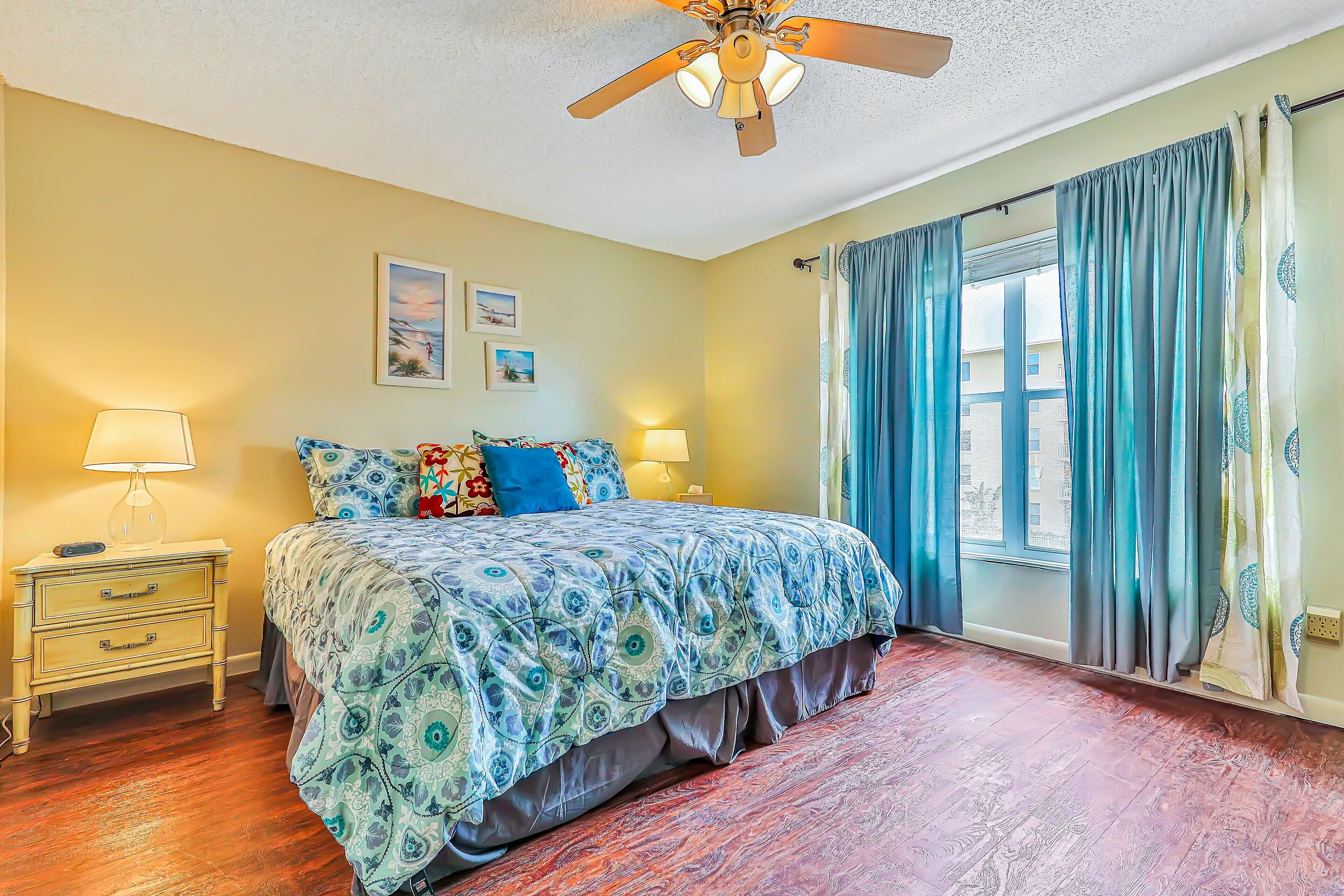 A bedroom with a bed, two bedside tables, a ceiling fan, and a window with curtains.