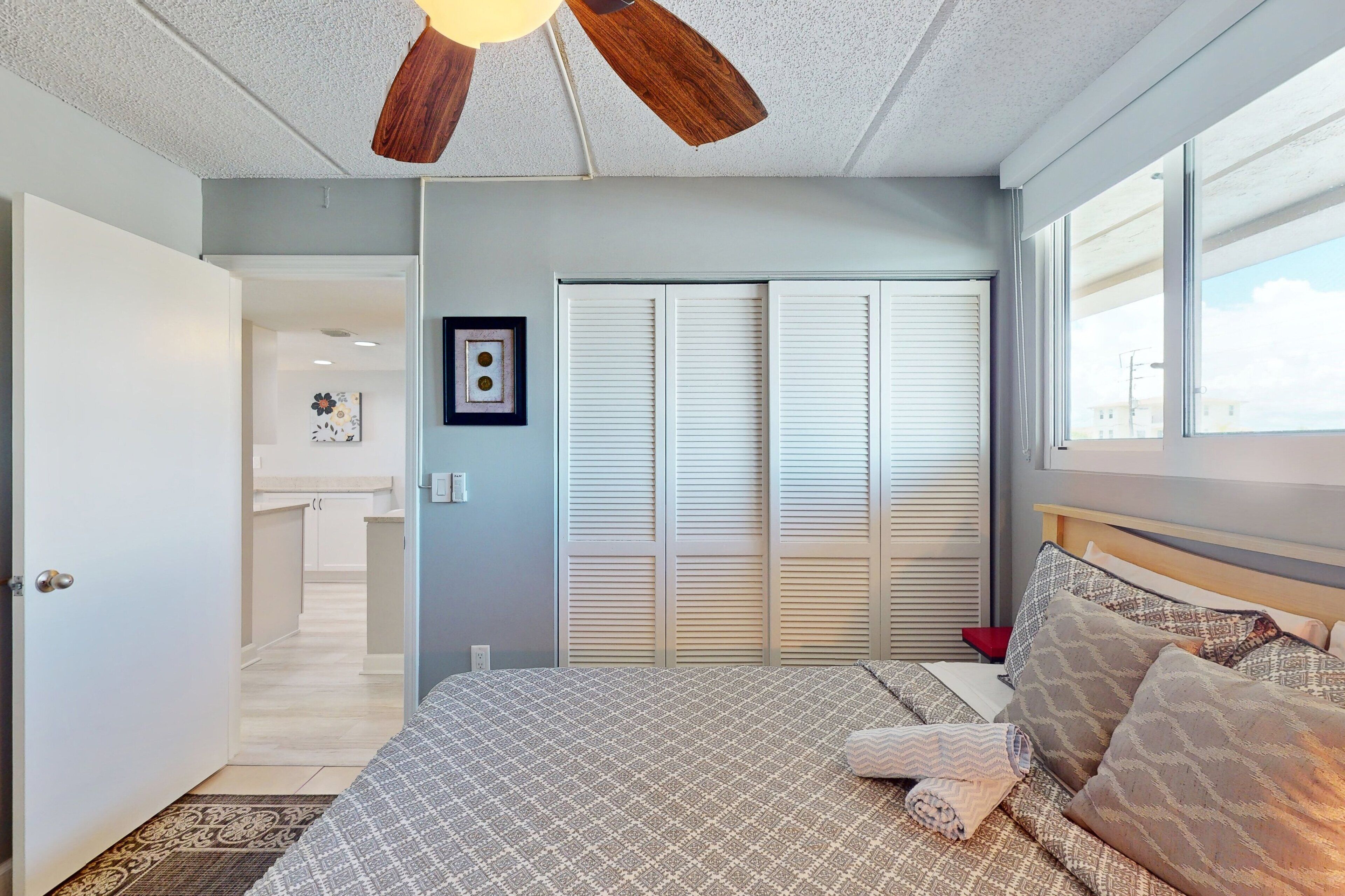 A bedroom with a bed, a ceiling fan, a window, and a door leading to a bathroom.