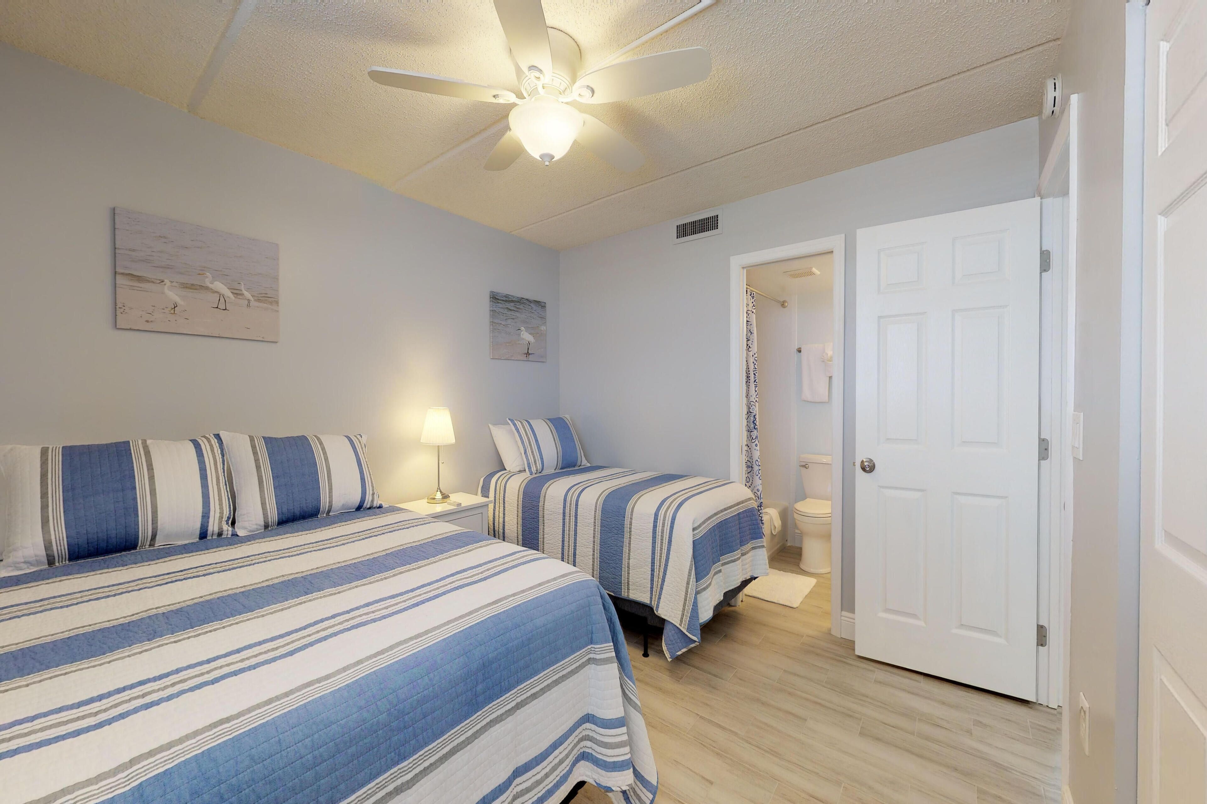 A bedroom with two beds, a ceiling fan, and a door leading to a bathroom.