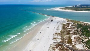 An aerial view of a beach with a long pier extending into the ocean, a sandy shoreline, and buildings in the distance. - Ponce Inlet (Ponce Inlet)