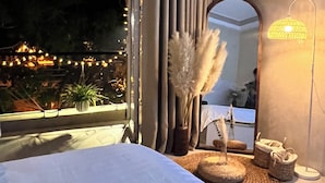 Een slaapkamer met een groot bed, een raam met gordijnen, een spiegel en een lamp.