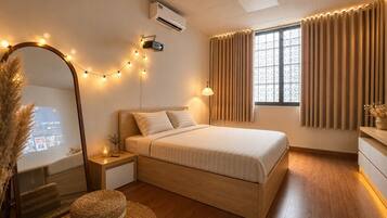 A bedroom with a bed, bedside table, lamp, mirror, air conditioning unit, window with curtains, and a projector screen.