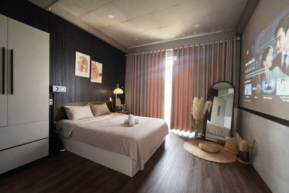 A modern hotel room with a large bed, a desk, a lamp, and a large mirror.