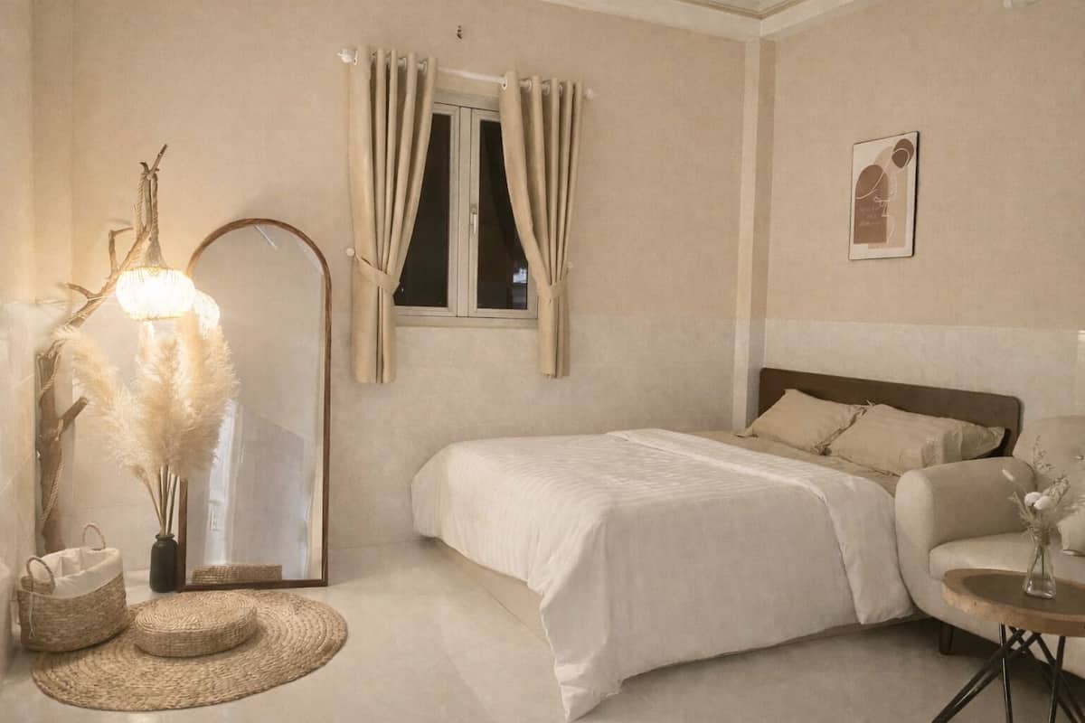 A bedroom with a bed, a chair, a small table, a lamp, and a window with curtains.