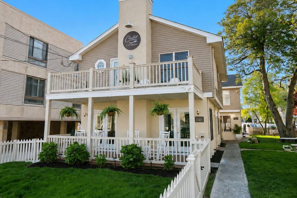 A two-story building with a balcony, a porch with potted plants, and a white picket fence.