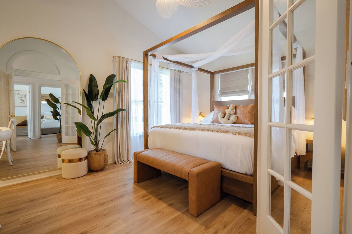 A bedroom with a wooden four-poster bed, a bench, a potted plant, and a view of a hallway.
