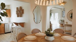 A dining area with a wooden table set for four, surrounded by wicker chairs, a hanging light fixture, and a large mirror on the wall. - Coastal Chateau Cottages (Ocean City)