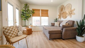A living room with a sofa, a chair, a large plant, and a wall with decorative items. - Coastal Chateau Cottages (Ocean City)