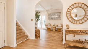 A spacious hallway with a wooden staircase, a large mirror, wicker furniture, and a sign reading 'Coastal Chateau'. - Coastal Chateau Cottages (Ocean City)
