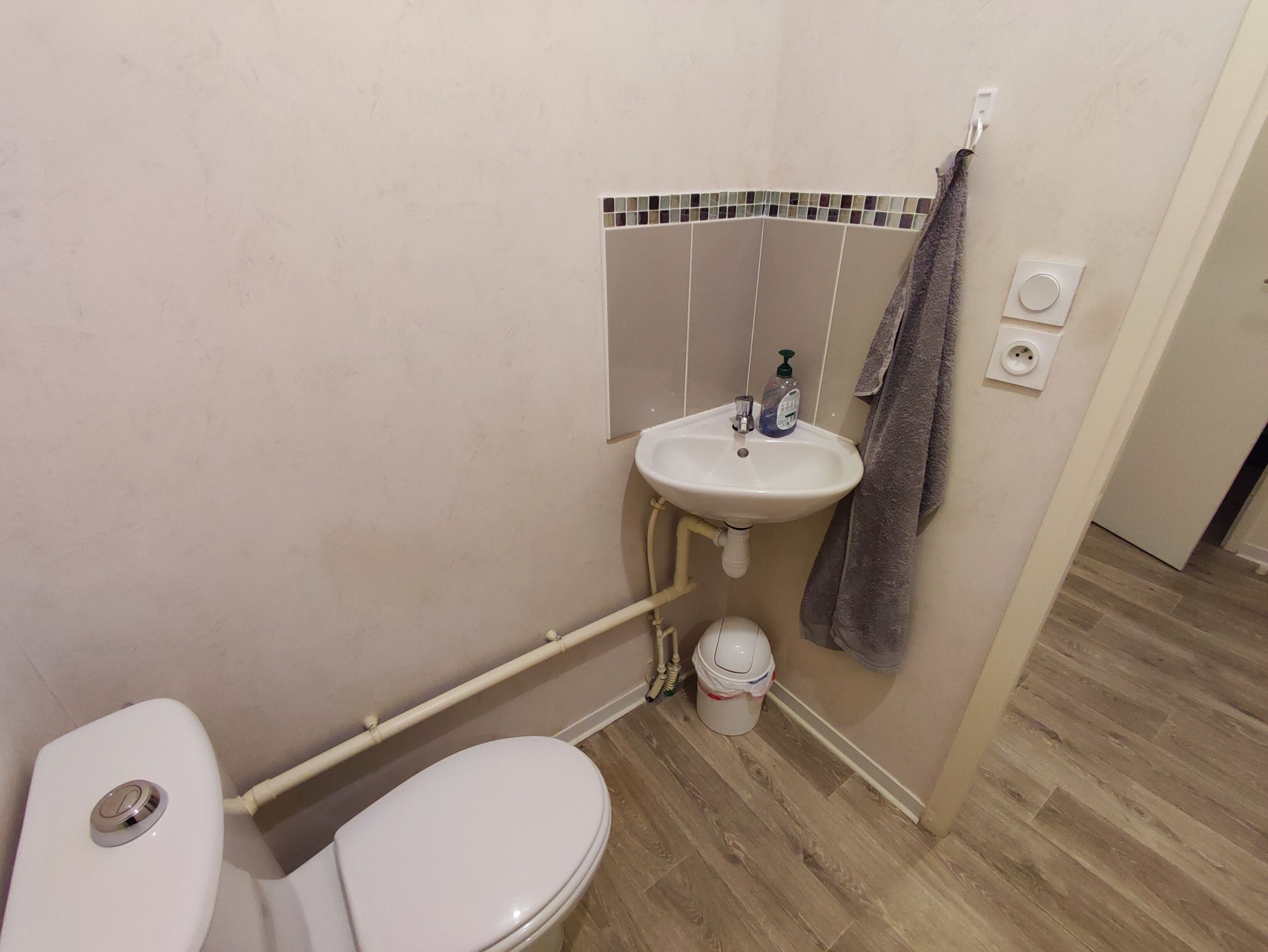 A small bathroom with a toilet, a sink, and a towel hanging on the wall.