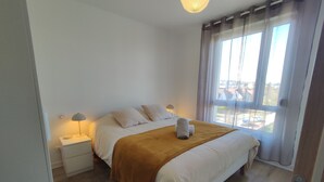 A bedroom with a bed, bedside tables, a lamp, and a window with curtains. - Duplex moderne, chaleureux au calme à Toison d'or (Dijon)