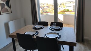 A dining area with a table set for four, a view of a balcony with a cityscape, and a framed abstract artwork on the wall. - Duplex moderne, chaleureux au calme à Toison d'or (Dijon)