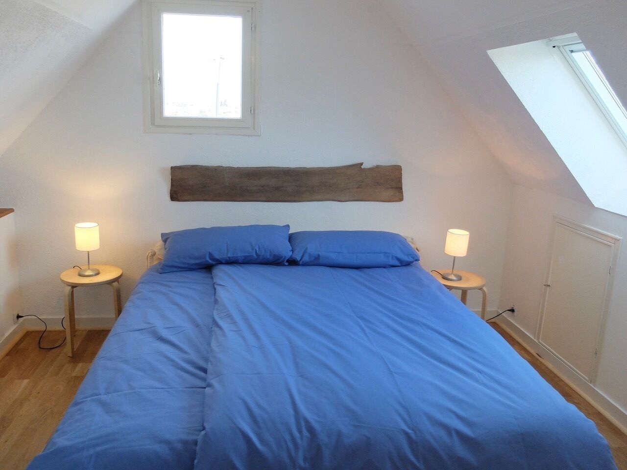 Ein Schlafzimmer mit einem großen Bett, zwei Nachttischlampen, einem Holzkopfteil und einem Dachfenster.