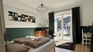 Ein modernes Schlafzimmer mit Bett, Schreibtisch und Stuhl. Ein Fenster mit Vorhängen bietet einen Blick nach draußen.