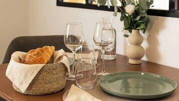 Une table à manger avec un panier tressé, une assiette verte, une serviette pliée et un vase rempli de fleurs.