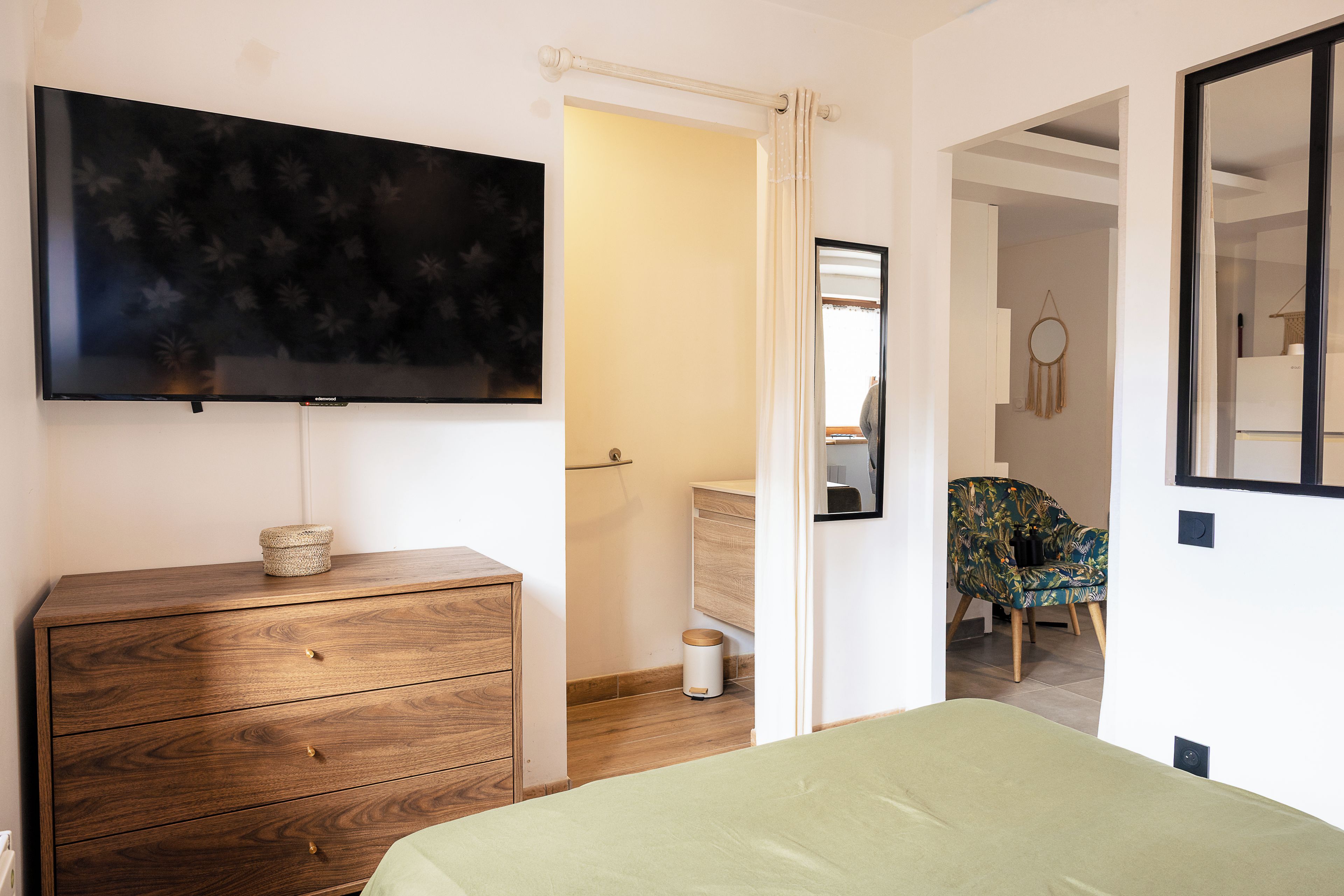 Ein Schlafzimmer mit einem Bett, einem Schminktisch, einem Fernseher und einem durchgehenden Türspalte einsehbaren Badezimmer.