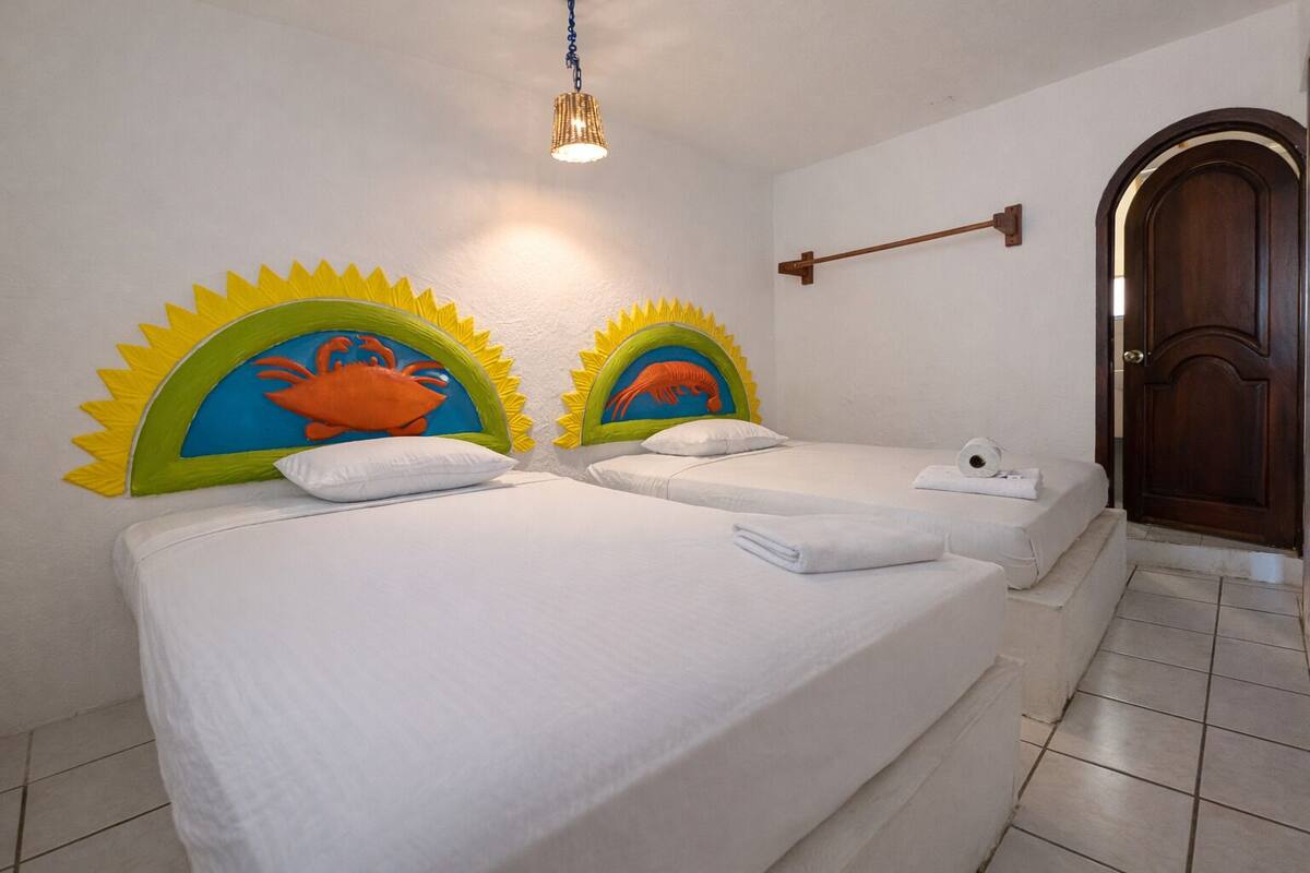 A double bed with white linens, two pillows, and a headboard with a sun and crab design.