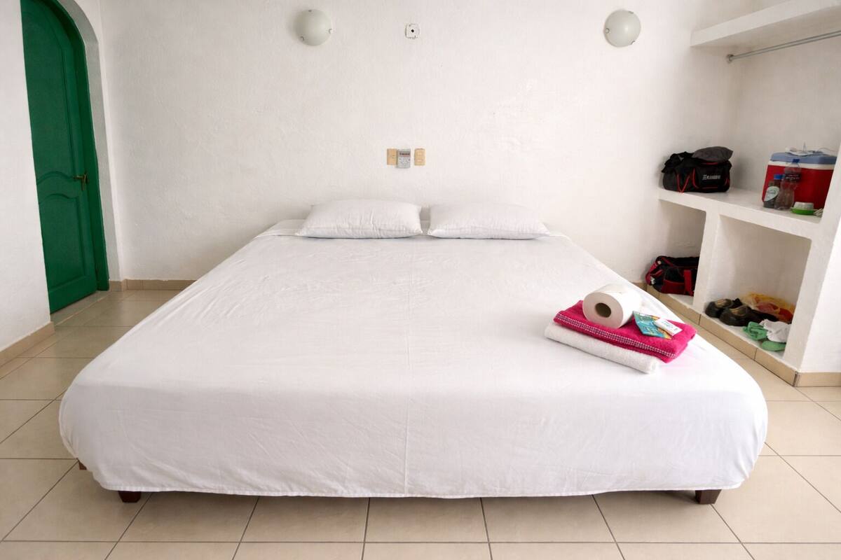 A neatly made bed in a room with a green door, a white wall, and a shelf with personal items.