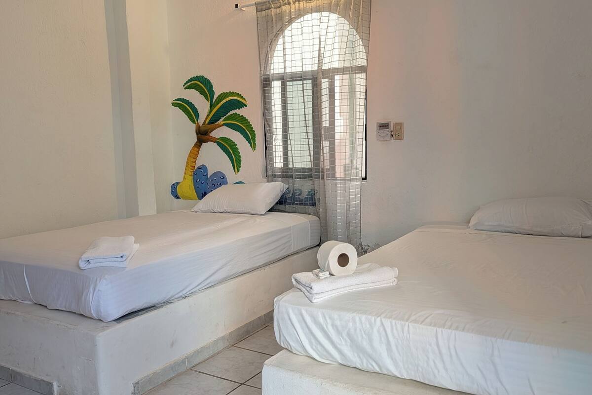 A room with two beds, white bedding, a window with a view, and a wall decoration.