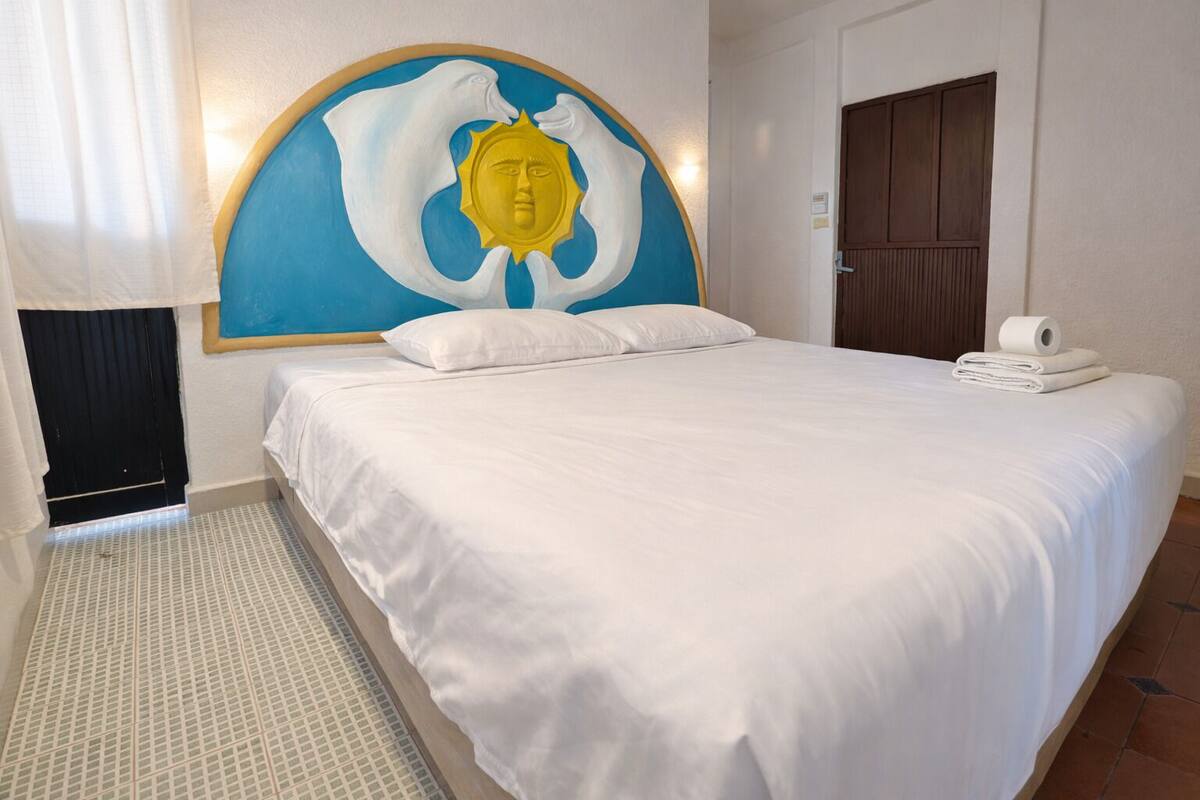 A hotel room with a large bed, a wall-mounted artwork, a door, and a roll of toilet paper on the bed.
