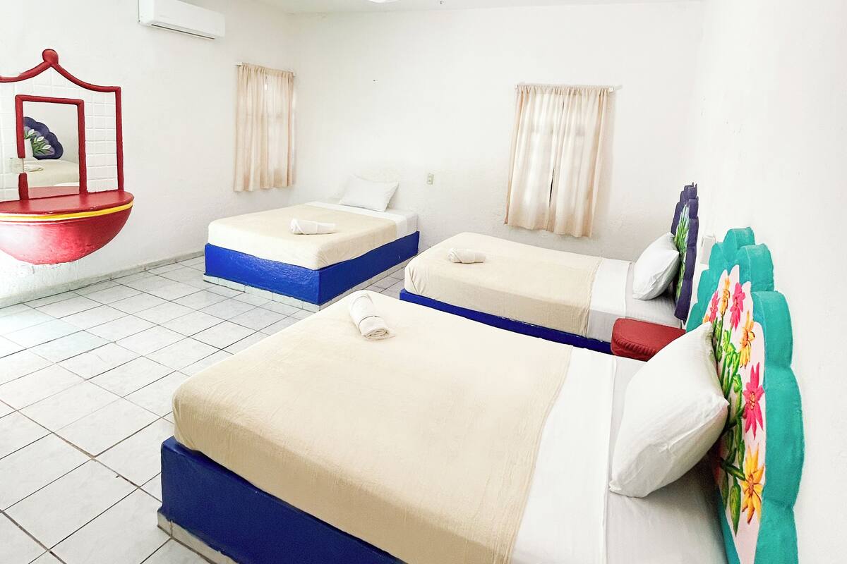 A hotel room with two beds, a ceiling fan, an air conditioning unit, and a window with curtains.