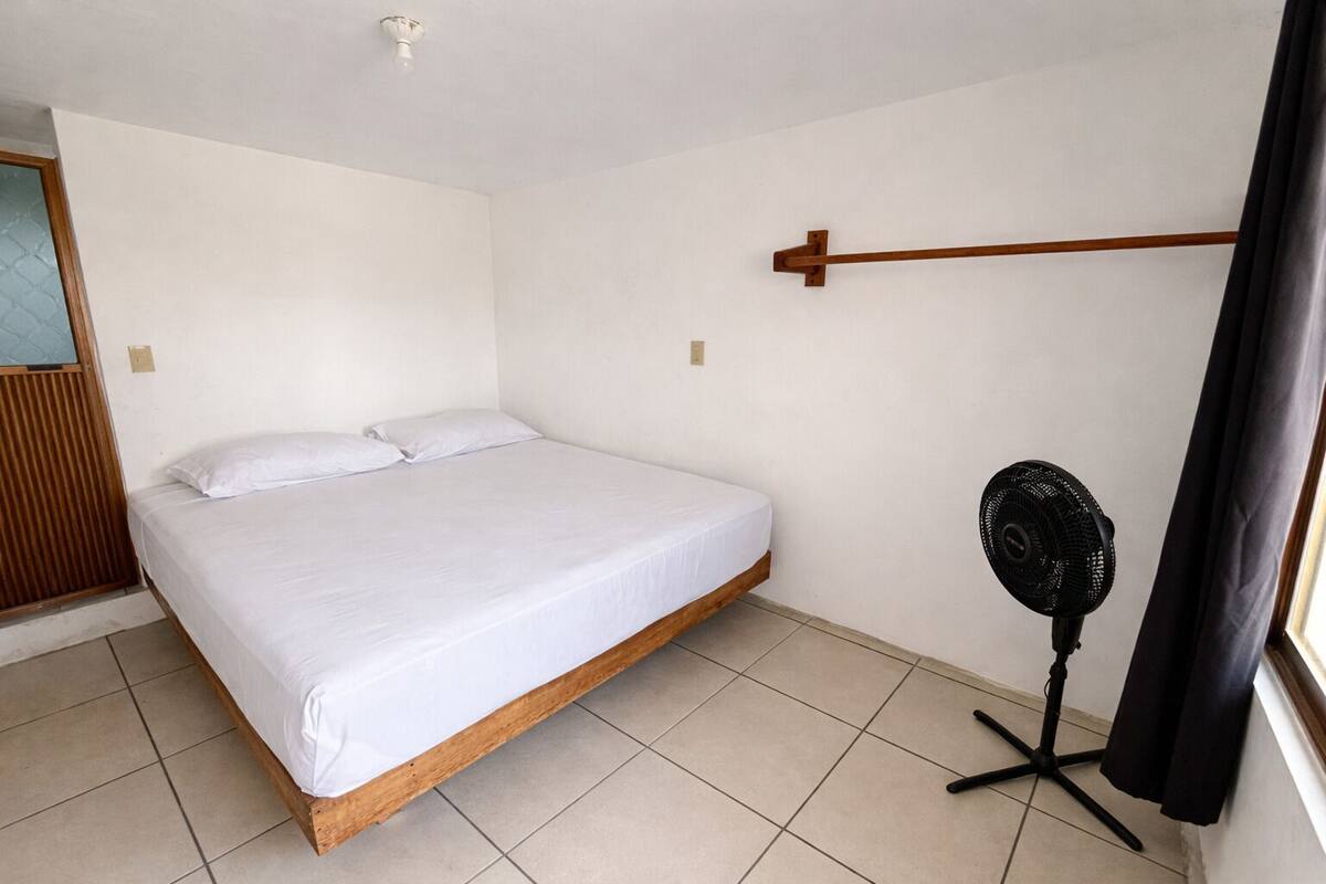 A single bed with a wooden frame and white bedding in a room with white walls and a tiled floor.