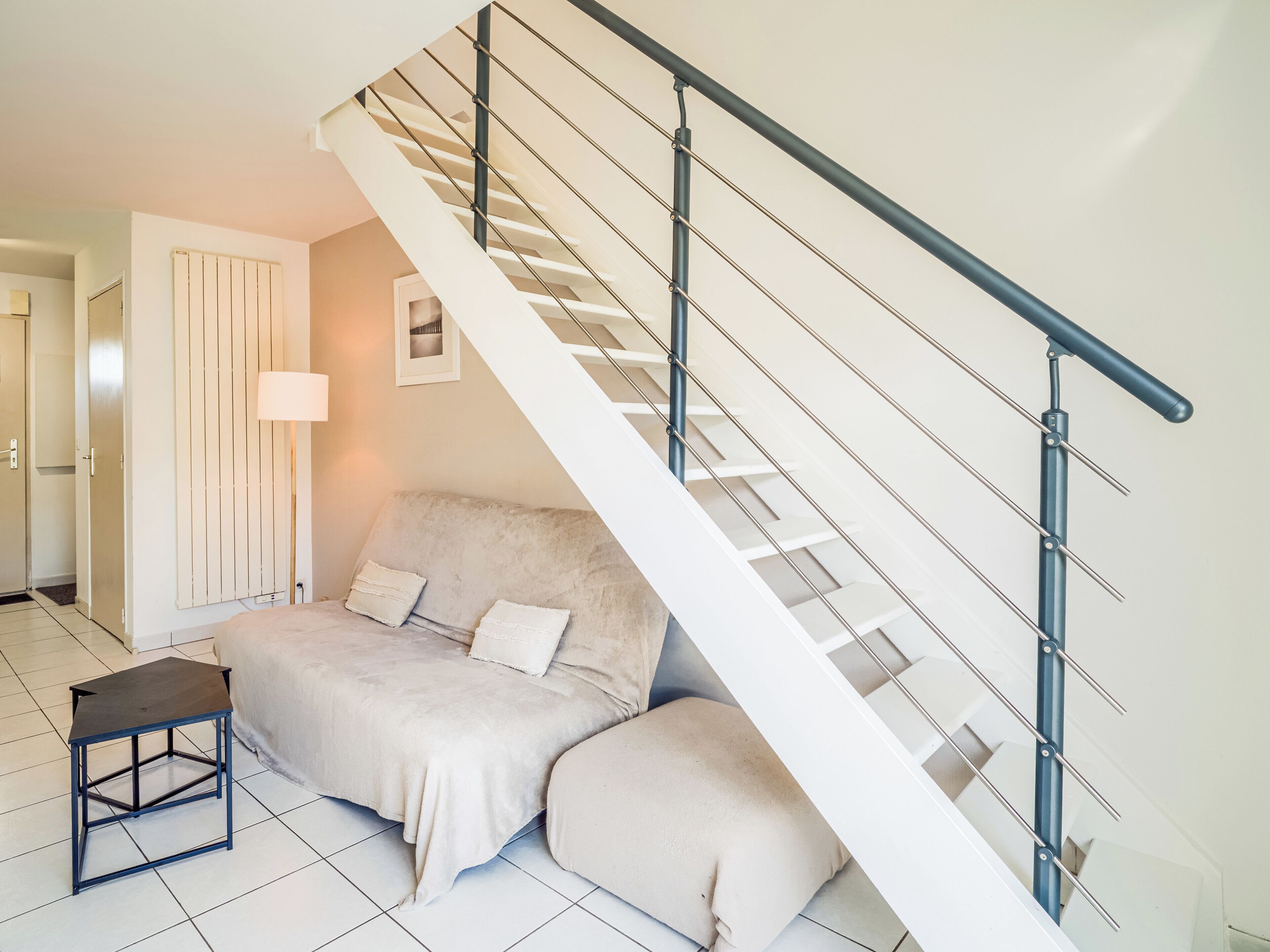 A modern living room with a sofa, a small table, and a staircase with metal railings.