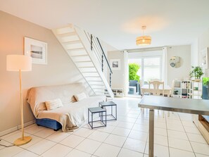Ein modernes Wohnzimmer mit einer Couch, einem kleinen Tisch, einer Stehlampe, einer Treppe und Blick ins Freie.