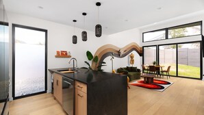Een moderne keuken met een centraal eiland, houten kastjes en een groot raam met uitzicht op een achtertuin.