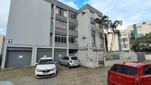 A multi-story residential building with numbered garage doors, a paved driveway, and parked cars. - Between the beaches (Florianópolis)