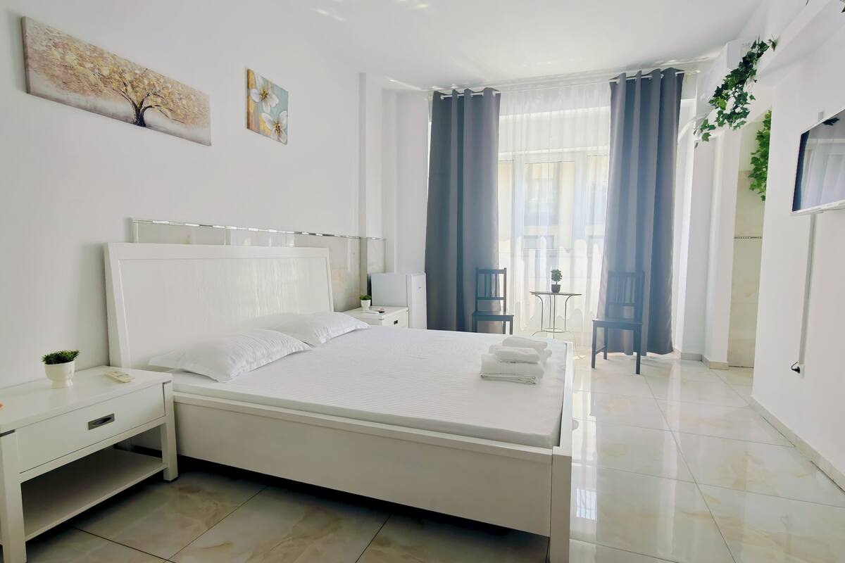 Un dormitorio moderno con una cama grande, una mesita de noche, una pequeña mesa con una planta y una silla.