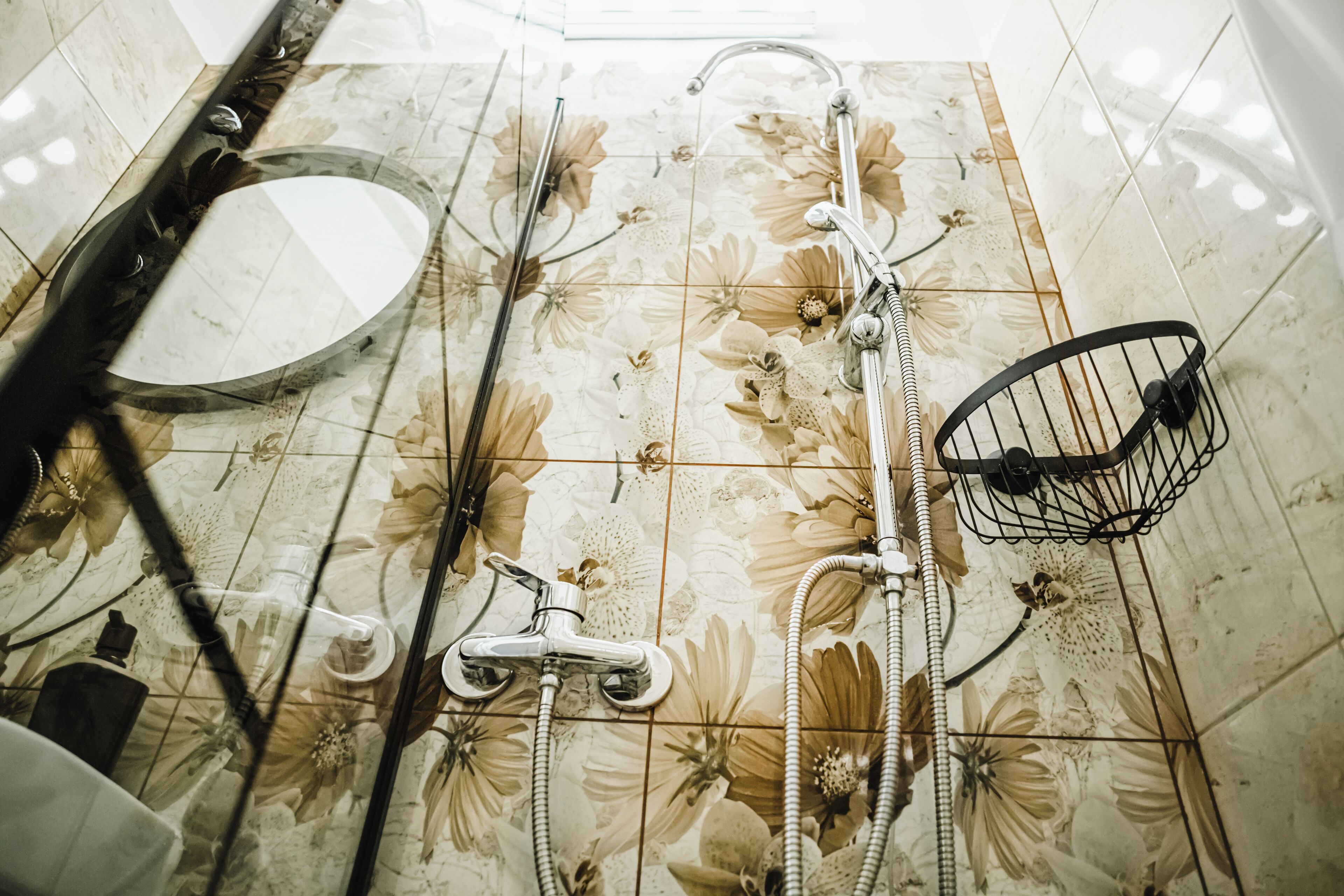 Un baño con resbalón de azulejos con motivos florales, un espejo redondo, una ducha con cabezal de ducha manual y un organizador de ducha de metal.