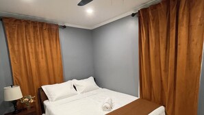 A neatly made bed with a white comforter and a brown throw blanket, a ceiling fan, and a nightstand with a lamp and a vase of flowers. - Beautiful 4-bedroom 2 bath residence. (Union)