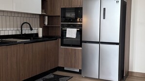 A modern kitchen with wooden cabinets, a stainless steel refrigerator, a built-in oven, and a black countertop. - Elegant 3-bed, 3-bath, located in the desirable neighborhood of Point E, Dakar (Dakar)