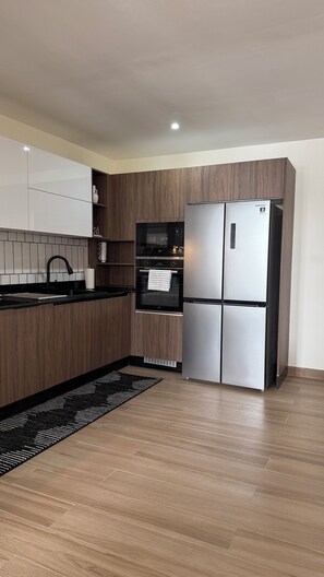 Una cocina moderna con armarios de madera, un refrigerador de acero inoxidable, horno integrado y encimera negra.