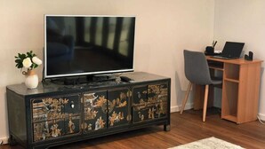Uma sala de estar com televisão, escrivaninha de madeira, laptop e um aparador decorativo.