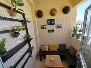 A small balcony with a black metal shelf holding potted plants, a black bench, and a small table with a woven mat. - F3 residential breezeway with sea view (Dakar)