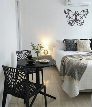 Habitación pequeña con cama, una mesa redonda con sillas, aire acondicionado instalado en la pared y una pieza decorativa de mariposa en la pared.