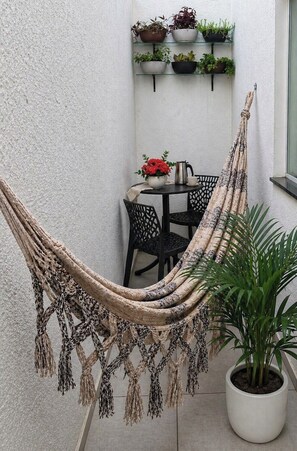 Una hamaca, una mesa con sillas y plantas en macetas en un espacio exterior pequeño.