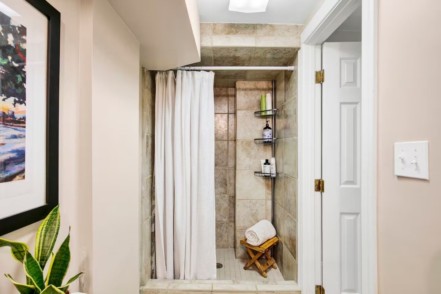 A bathroom with a shower, a towel rack, and a small stool.