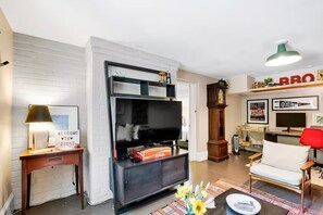 A living room with a TV, a clock, and a sofa. - Walkable 1-bedroom Five Points Gem with Style in Raleigh (Raleigh)