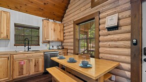 A log cabin kitchen with wooden cabinets, a wooden table with blue plates, and a bench. - Peaceful 3-Bedroom Cabin in Sevierville with Cozy Charm (Sevierville)