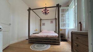 Ein Zimmer mit einem Himmelbett, einem runden Teppich, einer Kommode und einem Fenster mit Vorhängen.