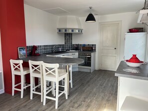 Una cocina compacta con una isla central, sillas blancas, una pared roja y un armario blanco.